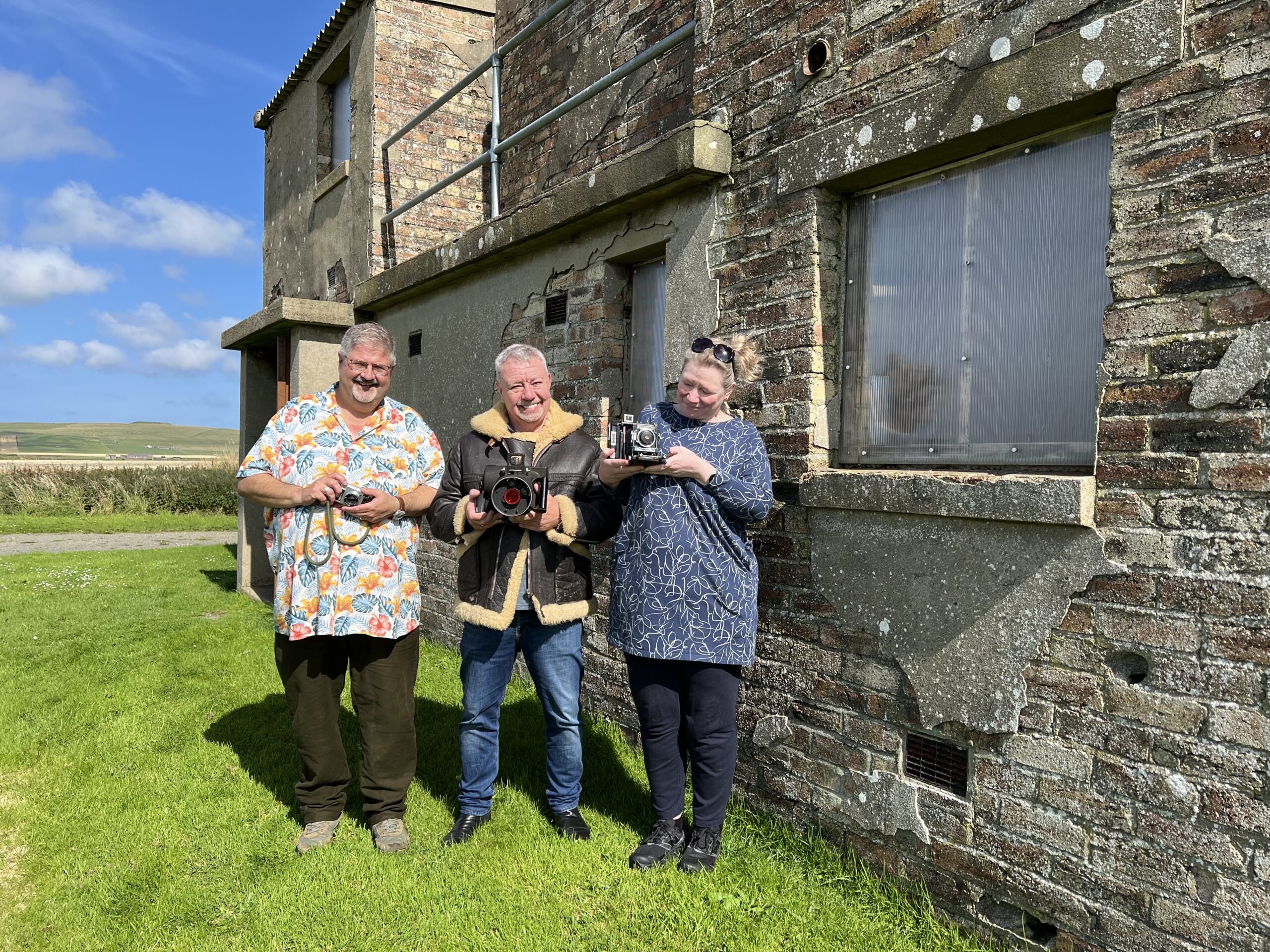 Three people standing in front of HMS Tern building with old camera equipment